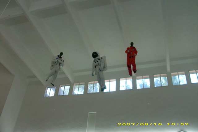 Three astronaut-suited figures suspended near the ceiling of a white interior.