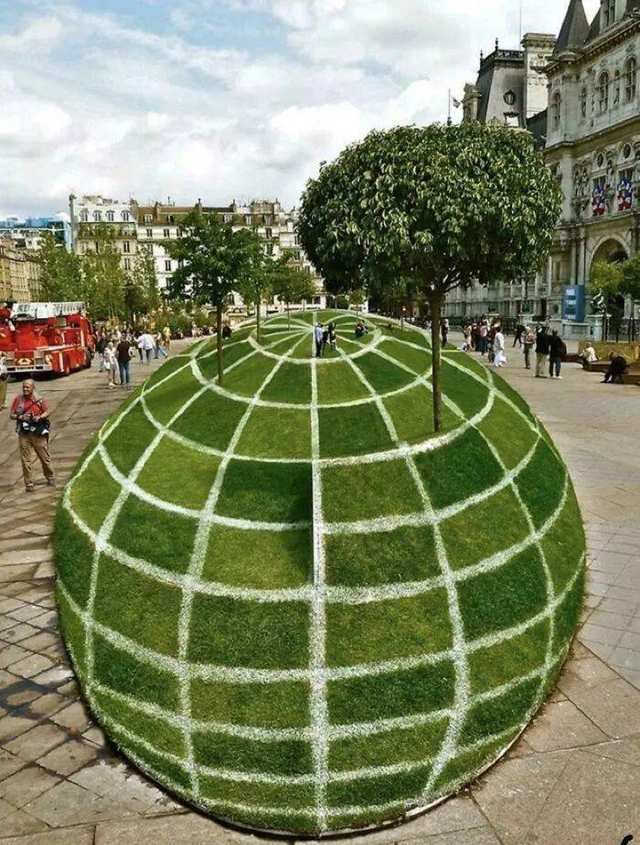 A green grass sphere painted with white grid lines in a public square.