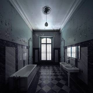 A decaying tiled bathroom with peeling walls, a bathtub, and two sinks.