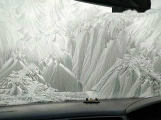 A car windshield covered in thick white frost that resembles jagged mountains and glaciers.
