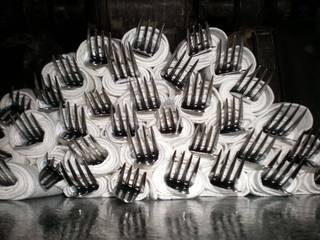 A white frosted cake covered in many upright metal forks.