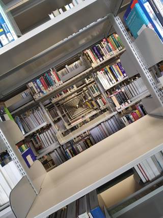 A library aisle photographed at a rotated angle, with bookshelves extending across the frame like walls.