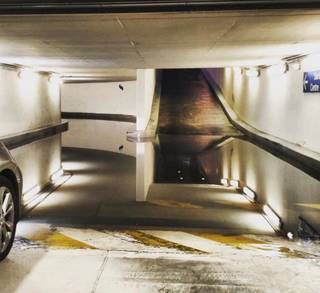 A large puddle in a parking garage reflects a ramp and ceiling, making the floor appear open.