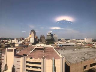 Ceiling lights reflected in a window appear as bright objects above a city in daylight.