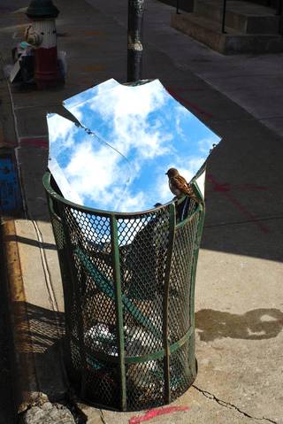 Mirror panels rest over a metal street bin and reflect blue sky and white clouds.