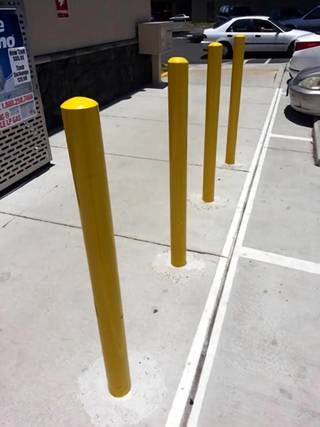 Several yellow safety bollards stand in a parking area with almost no visible shadows beneath them.