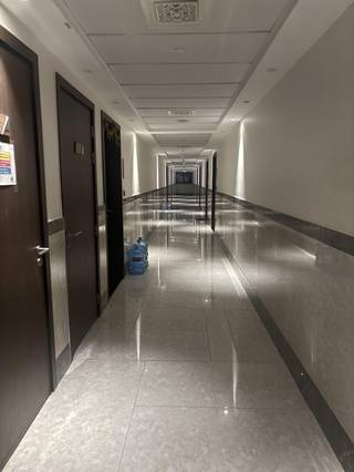 A long empty hallway with dark doors, glossy tiles, reflective wall panels, and water bottles.