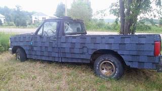 A parked pickup truck has blue asphalt roofing shingles attached across its hood, doors, and bed.