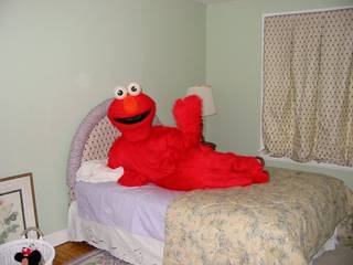 A bright red Elmo plush lies alone on a made bed.
