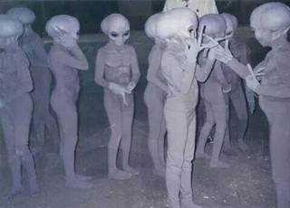 Pale alien figurines stand clustered together indoors.