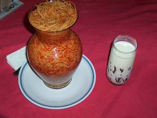 Spaghetti fills a decorative jar beside a drink.