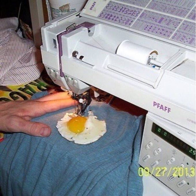 A sewing machine is positioned over a cracked egg on fabric.