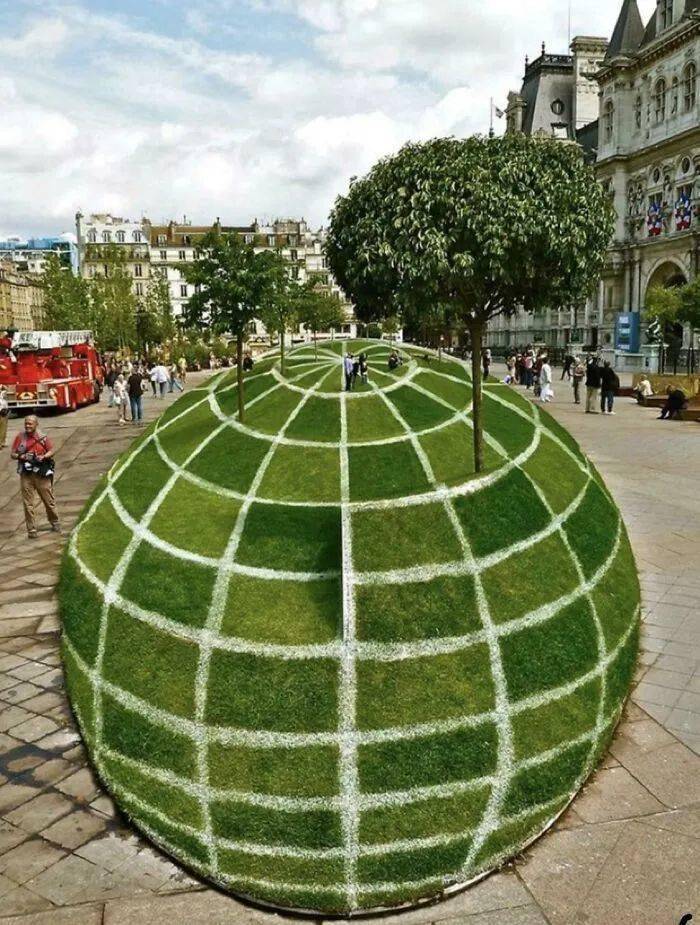 A green grass sphere painted with white grid lines in a public square.