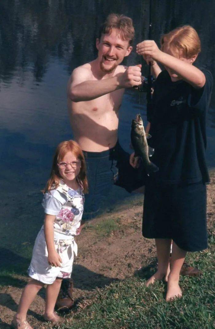Three people standing beside dark water in a low-resolution flash photo.
