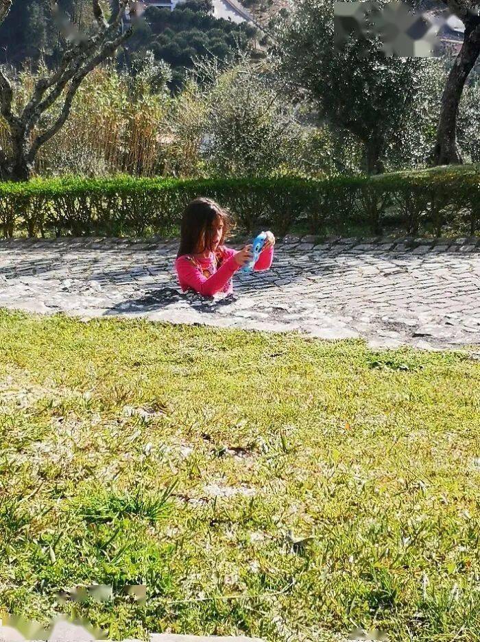 A red-clad person sitting alone near a path and hedge.