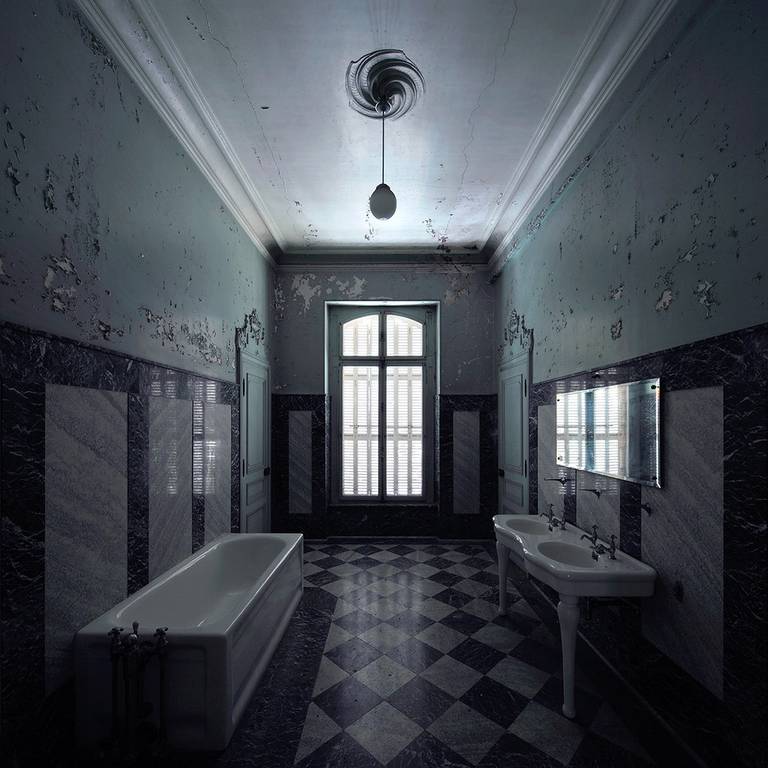 A decaying tiled bathroom with peeling walls, a bathtub, and two sinks.
