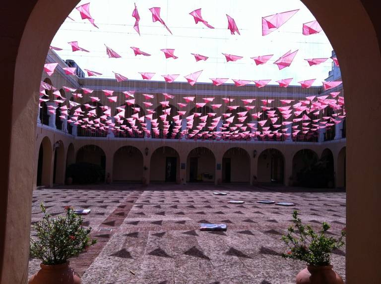 An arched courtyard with hundreds of small pink flags stretched overhead.