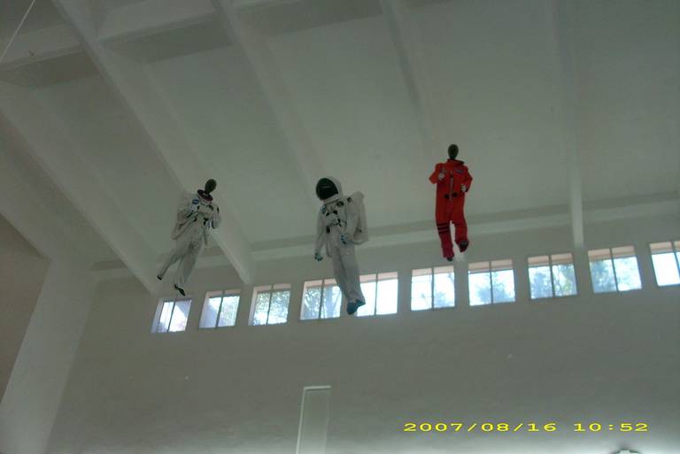 Three astronaut-suited figures suspended near the ceiling of a white interior.
