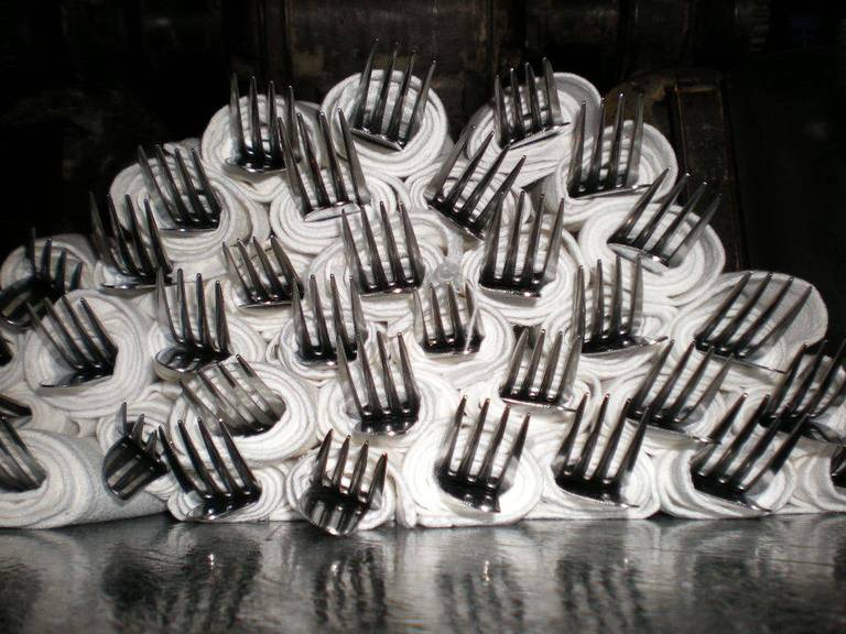 A white frosted cake covered in many upright metal forks.