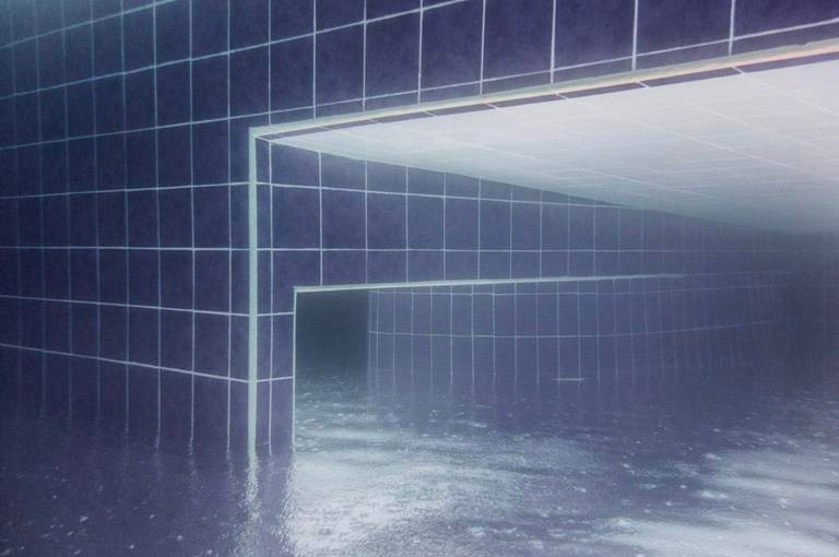 Blue tiled walls and rectangular openings seen through rippled water as empty flooded passages.