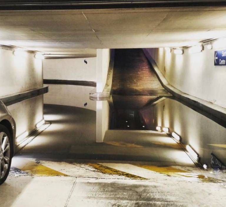 A large puddle in a parking garage reflects a ramp and ceiling, making the floor appear open.