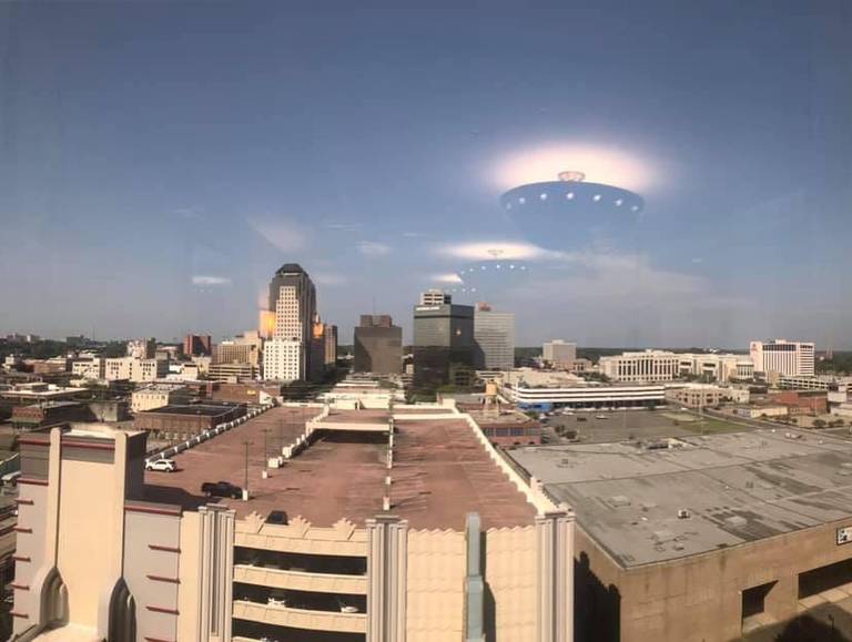 Ceiling lights reflected in a window appear as bright objects above a city in daylight.