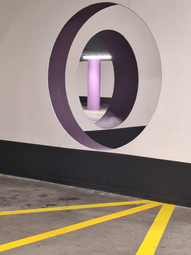 Two round openings aligned through parking-garage walls, with a purple column visible through both.