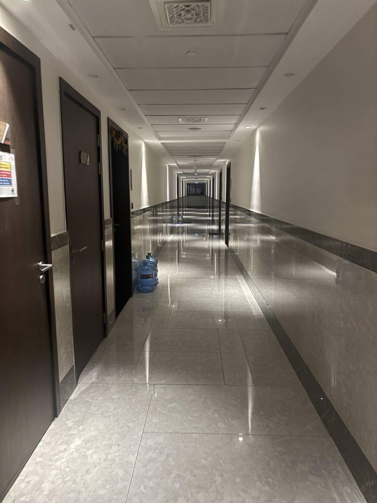 A long empty hallway with dark doors, glossy tiles, reflective wall panels, and water bottles.