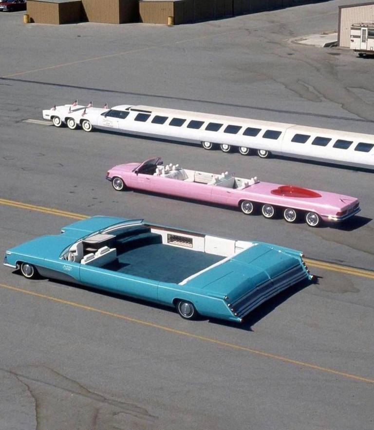 Three unusually elongated custom cars are parked on an open paved lot.
