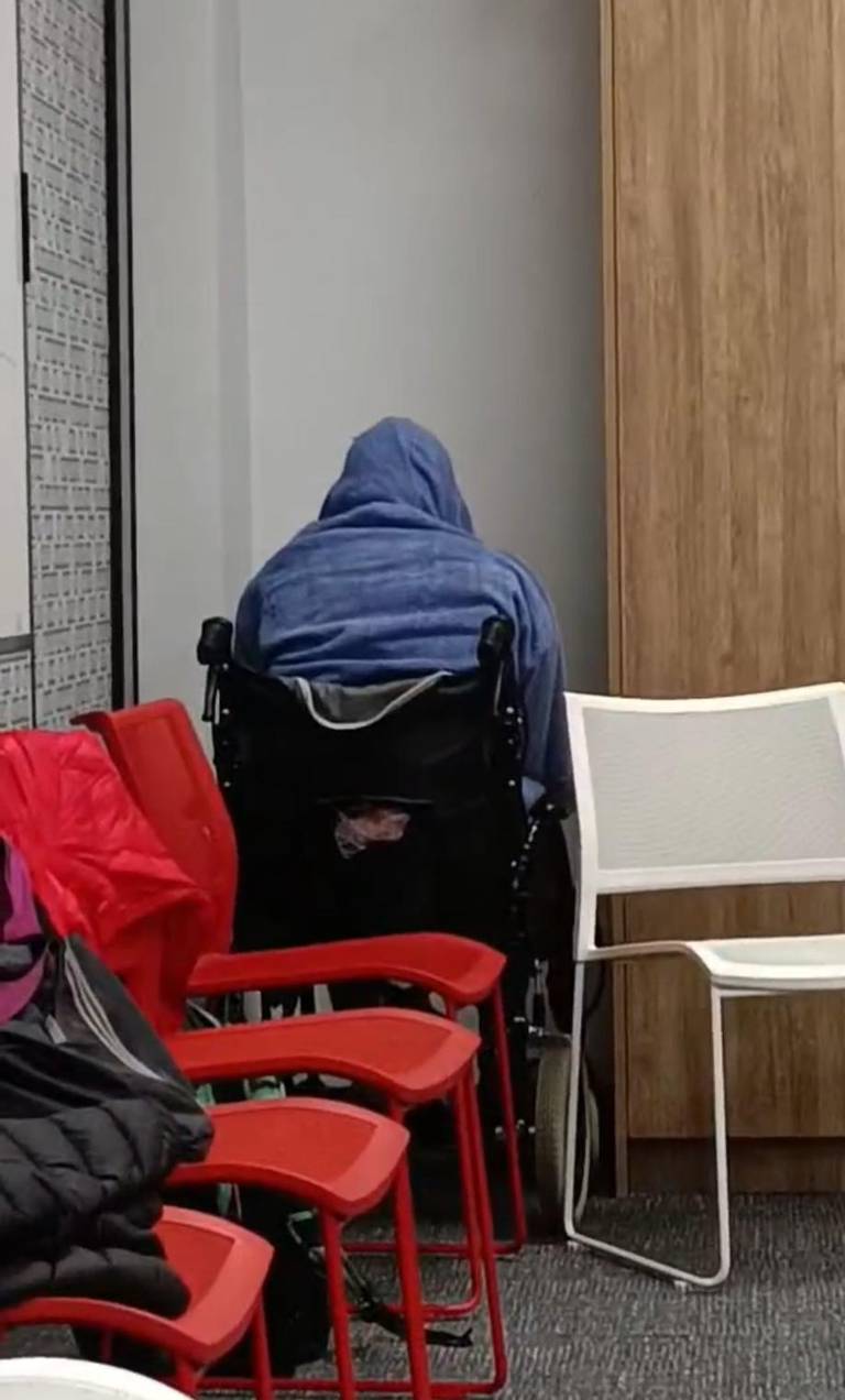 A covered CPR mannequin sits facing a corner behind stacked chairs.