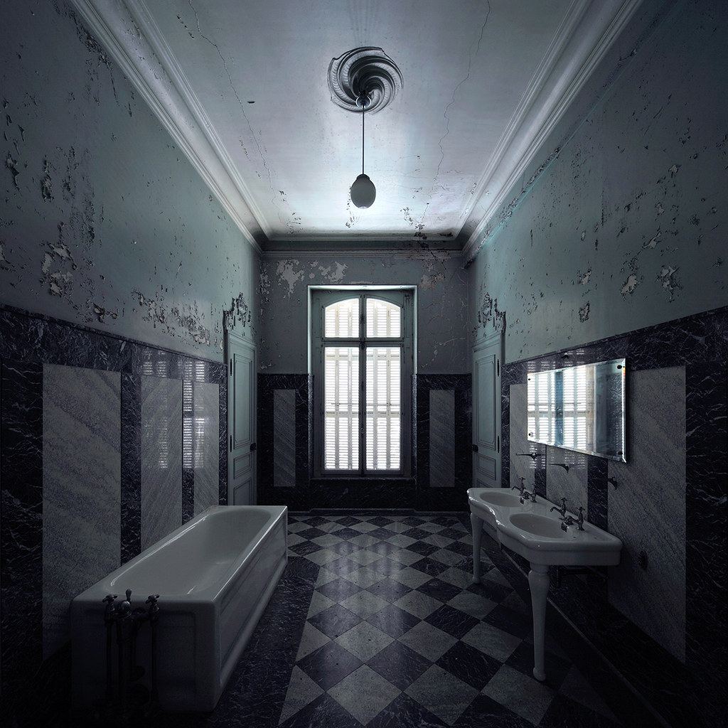 A decaying tiled bathroom with peeling walls, a bathtub, and two sinks.