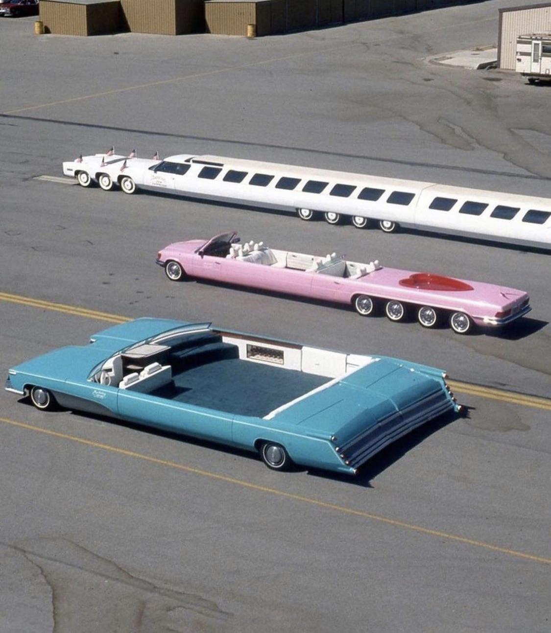 Three unusually elongated custom cars are parked on an open paved lot.