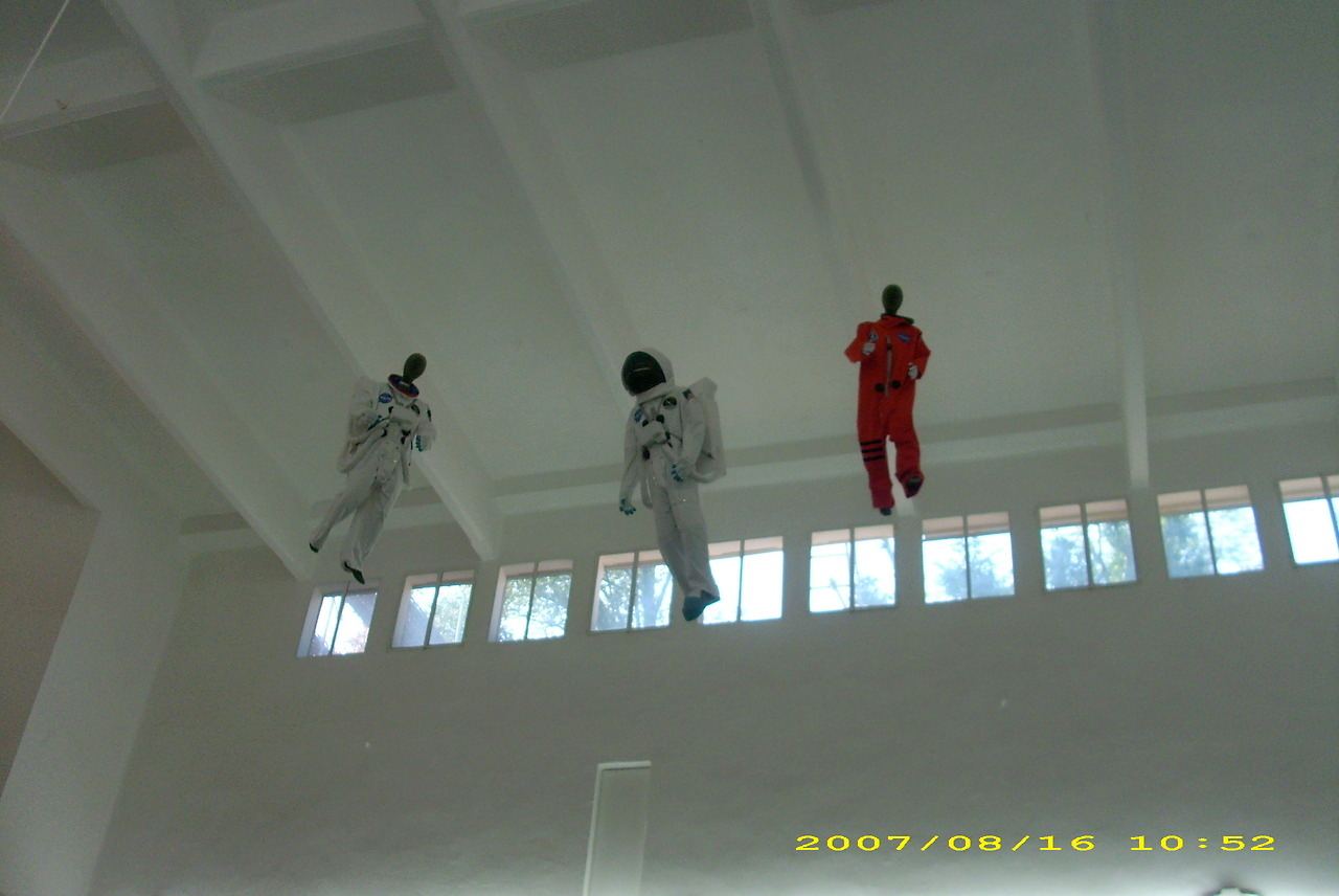 Three astronaut-suited figures suspended near the ceiling of a white interior.