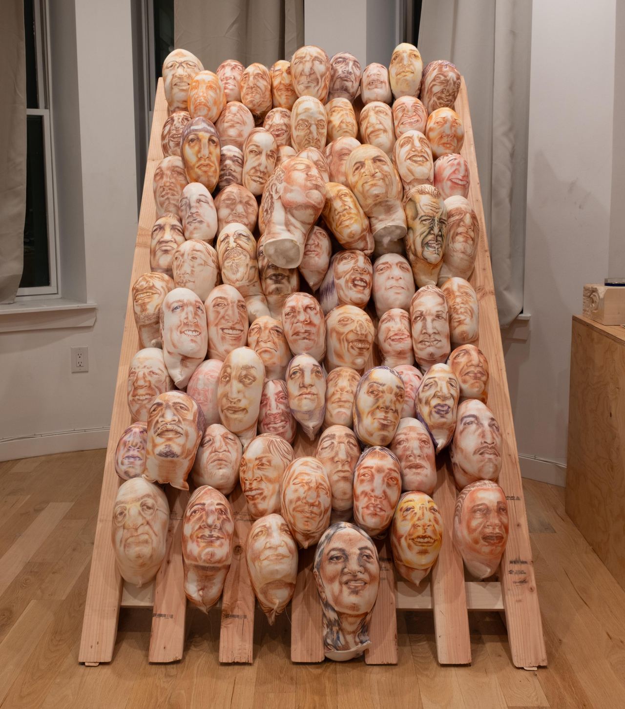 Rows of stuffed human-like heads are stacked on a frame indoors.