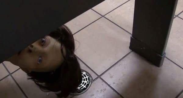 A doll head peers upward from a tiled floor drain or low opening.