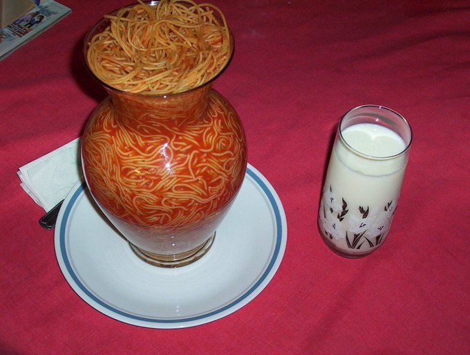 Spaghetti fills a decorative jar beside a drink.