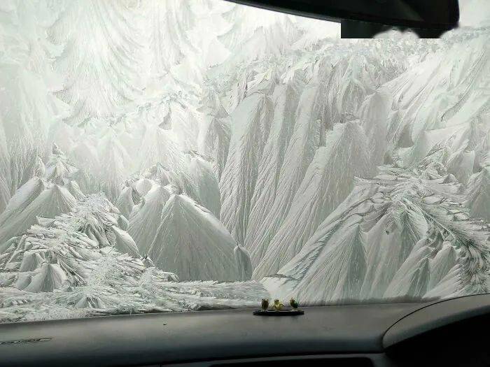 A car windshield covered in thick white frost that resembles jagged mountains and glaciers.