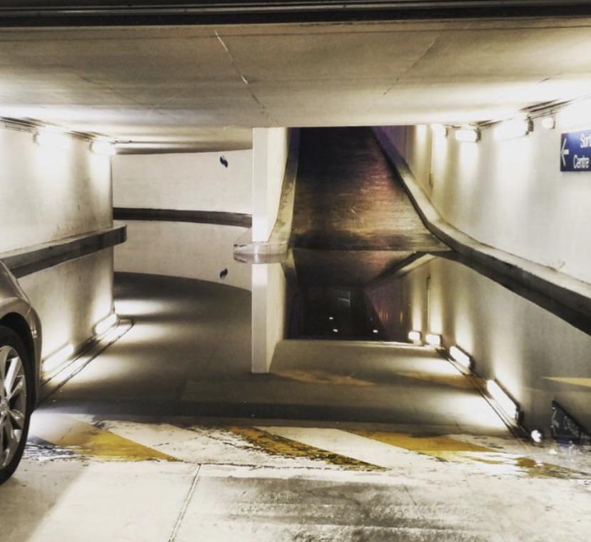 A large puddle in a parking garage reflects a ramp and ceiling, making the floor appear open.