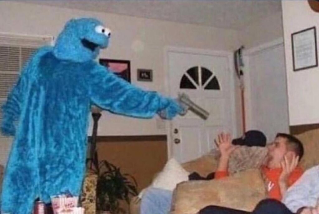 Cookie Monster Holds the Room Hostage: What’s Happening? 4 Man on a couch confronted by a Cookie Monster in costume with a gun.