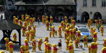 Hundreds of Winnie the Pooh mascots in a town square surrounding a police car.