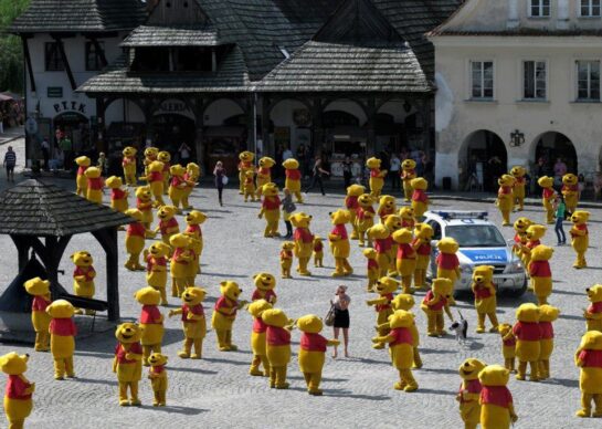 Hundreds of Winnie the Pooh mascots in a town square surrounding a police car.