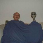 Unusual photo featuring a man and an alien in a living room.