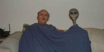 Unusual photo featuring a man and an alien in a living room.