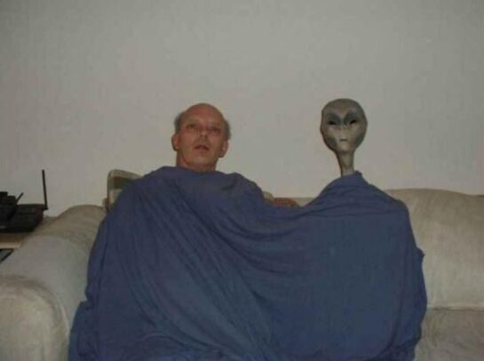Unusual photo featuring a man and an alien in a living room.