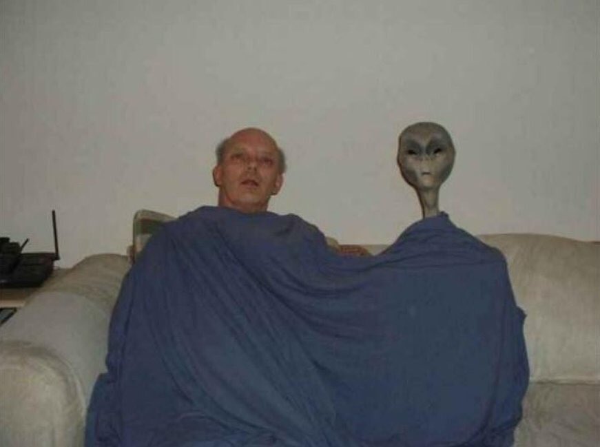 What’s Going on Here? Man and Alien Sharing a Blanket 4 Unusual photo featuring a man and an alien in a living room.