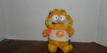 A damaged Garfield plushie with uneven eyes sitting on a table.
