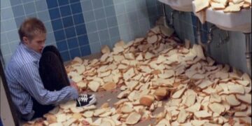 Man Sitting Among Slices of Bread in a Bathroom