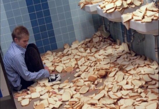 Man Sitting Among Slices of Bread in a Bathroom