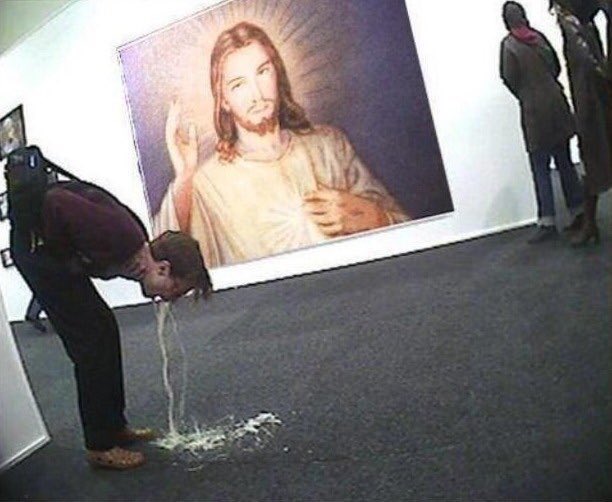 A man vomiting in an art gallery with a large Jesus portrait in the background.