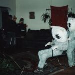 Two people dressed as cats, one pushing the other in a wheelchair.